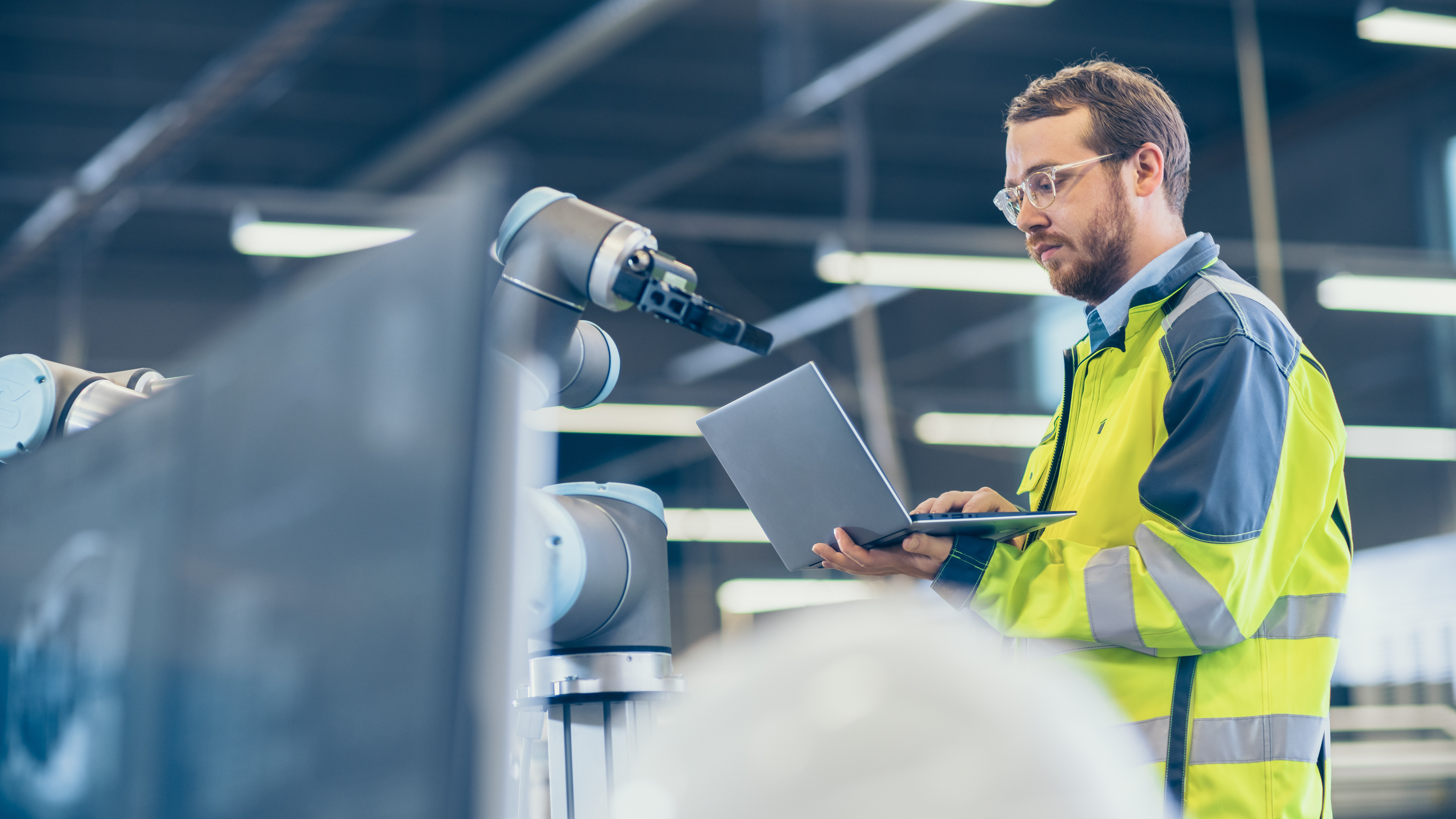 Automation Engineer Uses Laptop for Programming Robotic Arm.