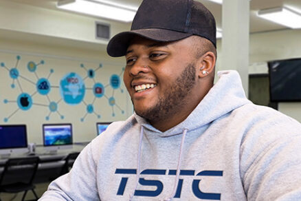 Student in a TSTC hoodie is using a computer and smiling happily.