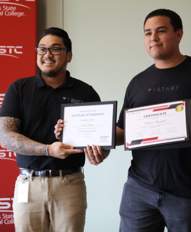 Micheal Jay and Victor Rangel stand side to side holding diplomas with a read TSTC backdrop on the left