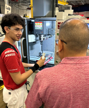 Francisco Garcia (right), a TSTC Precision Machining Technology instructor, explains how to place an aluminum part in a CNC mill to Matthew Montiel, a recent graduate of the South Texas ISD Science Academy, during the ACE CNC training bootcamp hosted at TSTC.