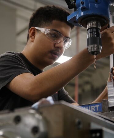 Ortiz wearing a black shirt and safety glasses works with a CNC machine