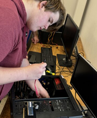 Jacob Hosterman wears a burgandy hoodie holding computer and looking at the ports of the wire.