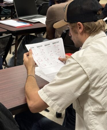 New structural welding student wearing a black baseball cap looks at a handout explaining four types of welds.