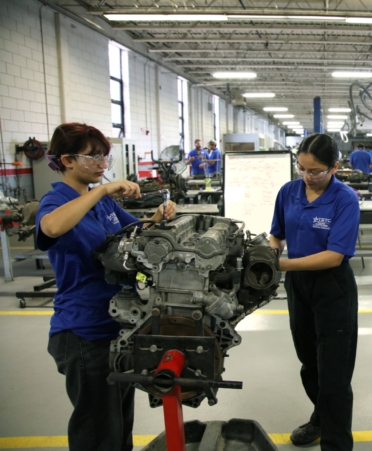 Four women wearing blue TSTC polo shirts work on two engines in a lab.