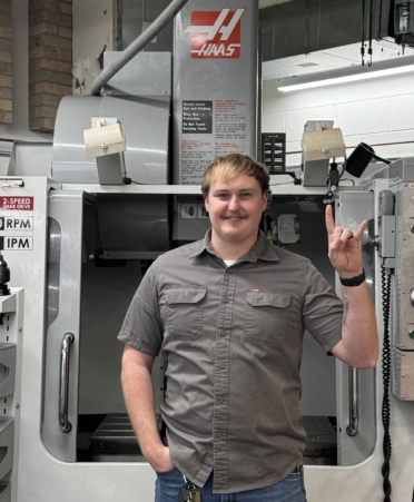 TSTC Precision Machining Technology alumnus Chris Gamble stands in front of a CNC tool at the University of Texas at Austin’s machine shop, where he works. (Photo courtesy of TSTC.)