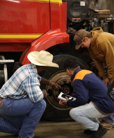 Three students gather around a diesel truck tire.