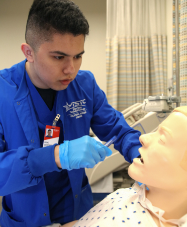 nursing student in blue lab coat working with medical manikin