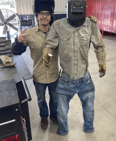 Man in khaki shirt standing next sculpted scarecrows