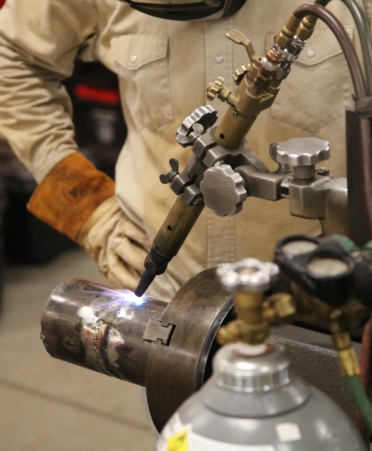 A student welds a pipe in while wearing protective gear.