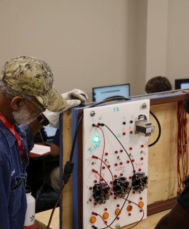 A student and instructor work on a board with various colored wires.